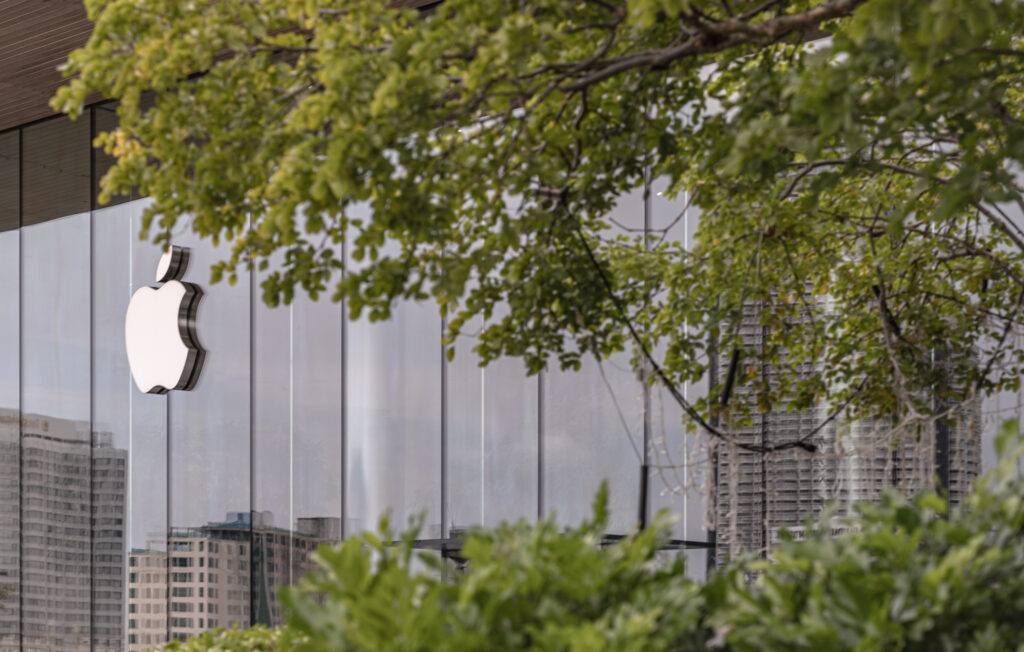 Modern stylish logo sign attached to glass wall with reflections of high building at Apple store