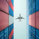 Tall stacked shipping containers with a plane flying above