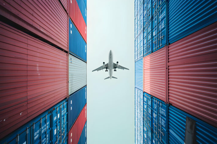 Tall stacked shipping containers with a plane flying above
