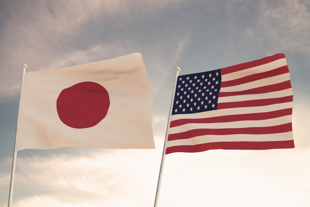 US and Japanese flags waving against a cloudy sky