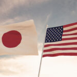 US and Japanese flags waving against a cloudy sky